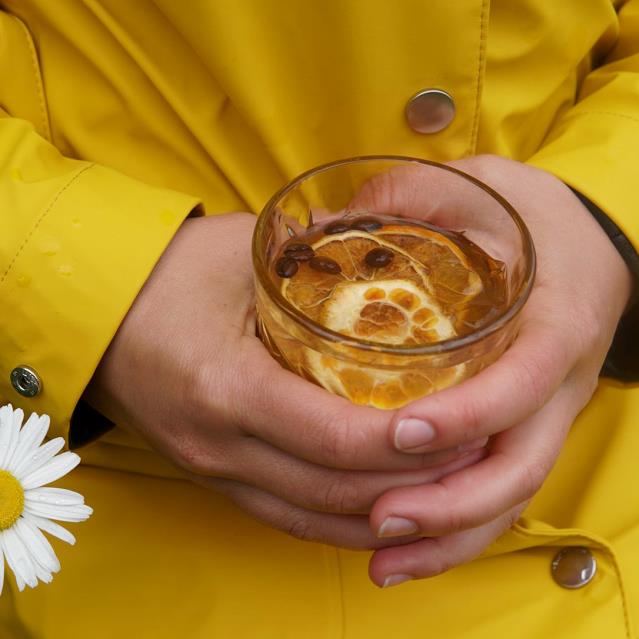 gul jakke, hænder, glas med tonic og appelsinskive